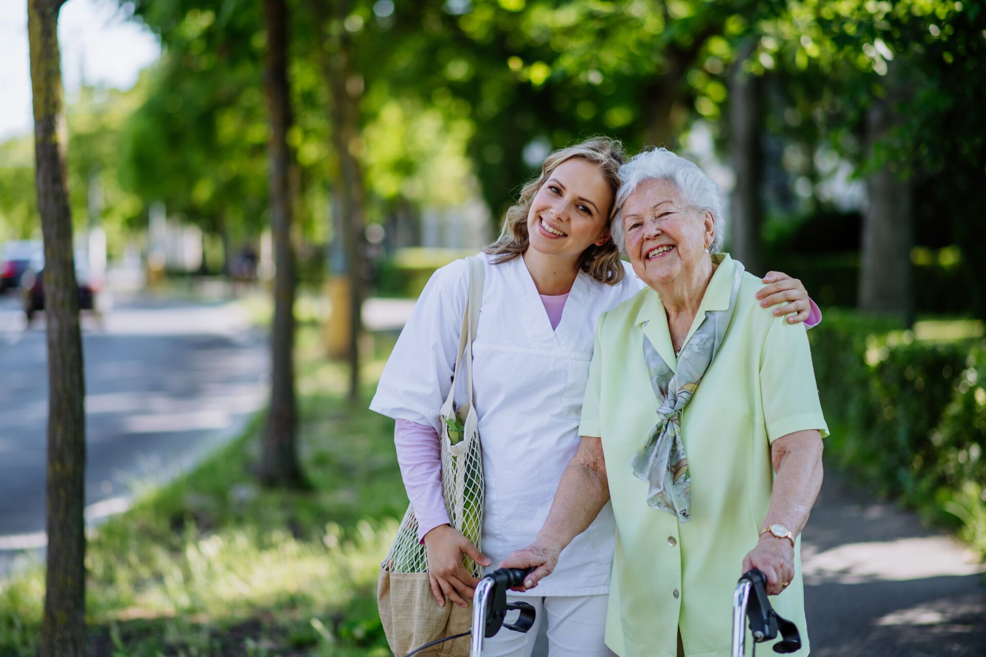 Eine Krankenschwester nimmt eine ältere Dame in die Arme und Sie gehen zusammen spazieren im park